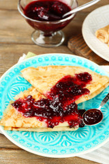 Delicious pancakes with berry jam on plate on wooden background