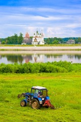 Farmer mowing against church and river, Russia