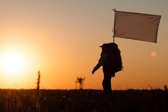 Hiker with backpack and flag walking in the field