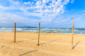 Fototapeta na wymiar Wooden poles on sandy Can Picafort beach, Majorca island, Spain