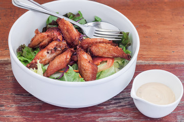 Dressing salad with fried chicken wing in white bowl