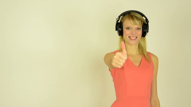woman listens to music with headphones and shows a thumb up to