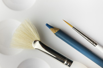 Artists paintbrushes and blue pencil on white pallete background