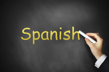hand writing spanish on black chalkboard