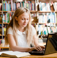 pretty female student typing on notebook in library