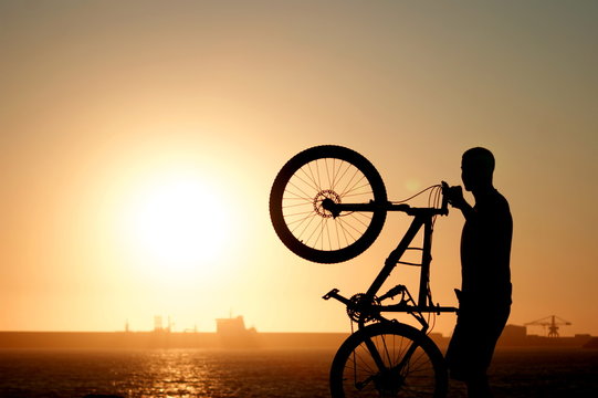 Boy holding a mountain bike against the setting sun