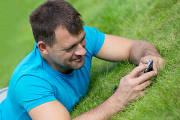 Man lying on grass with mobile smart phone and writing sms