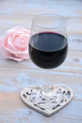 Fototapeten glas rode wijn op houten tafel met hart decoratie en roze roosje © trinetuzun