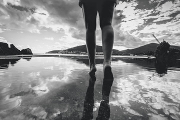 Monochrome photo of female legs walking on water with sky reflec
