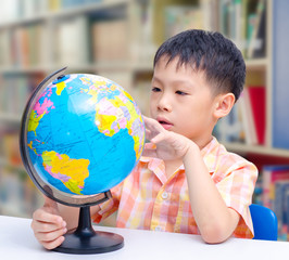 Asian boy looking at a globe in library