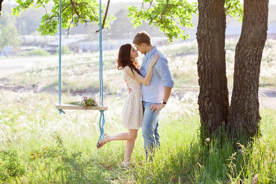 Young Kissing Couple Under Big Tree With Swing