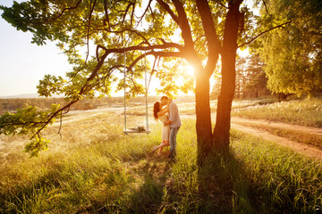 Young kissing couple under big tree with swing at sunset - Powered by Adobe