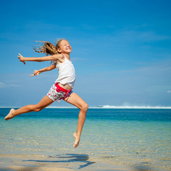 Naklejka premium teen girl jumping on the beach at blue sea shore in summer vaca