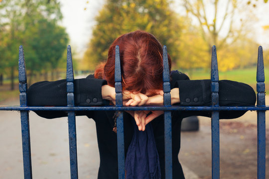 Sad woman leaning on gate in park