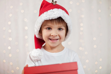 Smiling funny child in Santa red hat holding Christmas gift in h