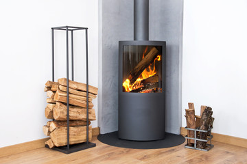 Obraz premium Photo of a fire in a modern burning stove next to a wood logs rack, contemporary home log burner or fireplace, renewable energy heating in winter