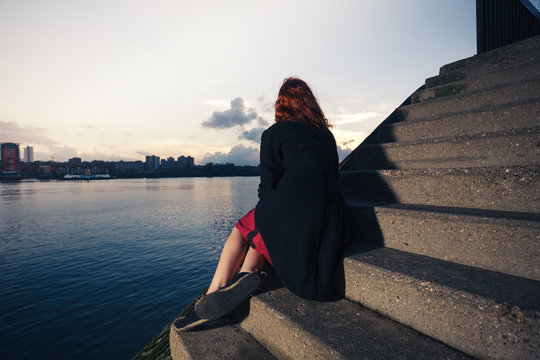 woman sitting on stairs by river at sunset