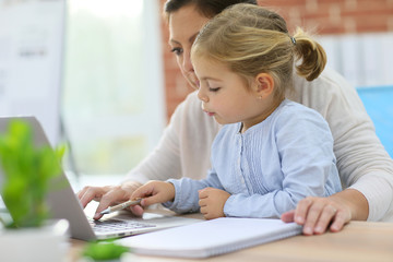 Mother working at home-office with daughter on her lap