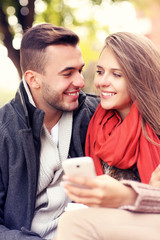 Joyful couple on a bench with smartphone in the park
