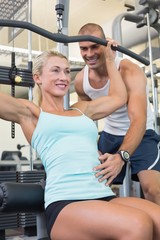 Male trainer assisting woman on a lat machine in gym