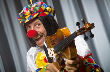 Funny clown plyaing violin against curtain