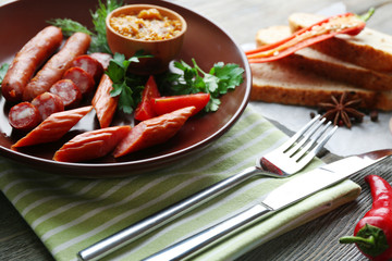 Assortment of tasty thin sausages on plate on wooden background