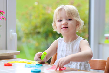 Blonde toddler girl making cookies from plasticine