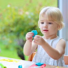 Blonde toddler girl making cookies from plasticine