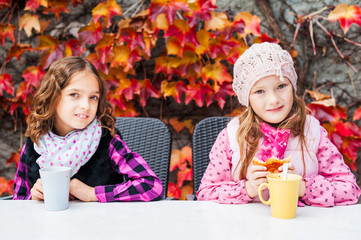 Adorable little girls drinking hot chocolate on a terrace