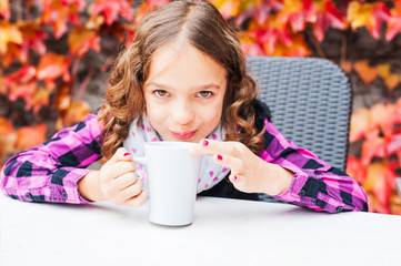 Cute little girl drinking hot chocolate on a terrace