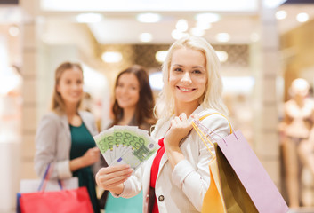 young women with shopping bags and money in mall