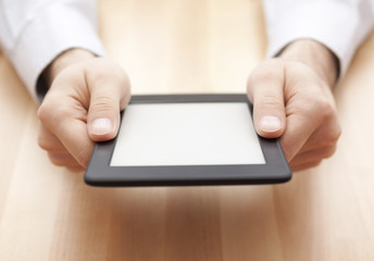 Tablet or e-book reader in hands on wood background
