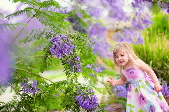 Cute happy little girl in blooming park. Beautiful Jacaranda