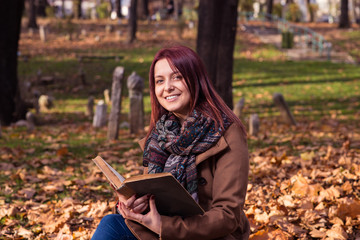 Obraz premium redhead girl sitting on bench in park and reading book