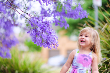 happy little girl has a fun in blossom jacaranda garden