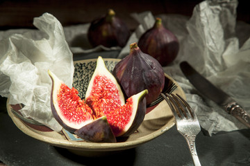 cut fresh figs on a ceramic plate, with silver fork and knife -