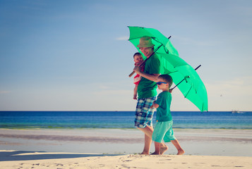 father and kids with umbrellas on beach vacation