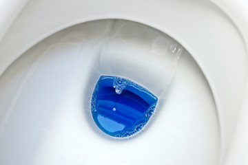 Close up of a white toilet bowl with blue cleaning product