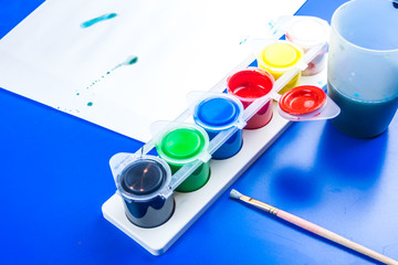 child is painting a picture with tempera paints on blue table