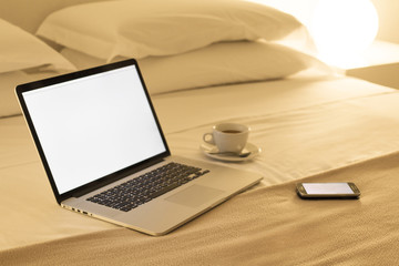 Computer,cell phone and coffee on the bed.