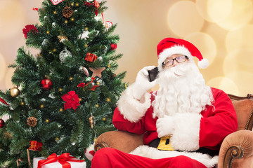 santa claus with smartphone and christmas tree