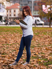 Redhead girl standing and reading a book in park
