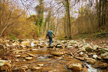 Hiker man crossing a river on stones