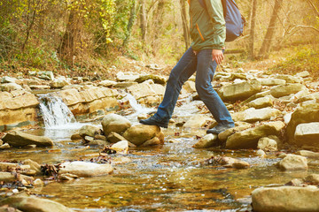 Hiker man crossing a river on stones, view of legs