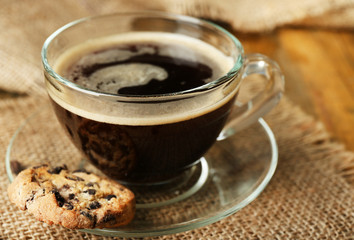 Glass cup of coffee and tasty cookie on wooden background