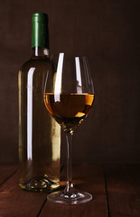 Wine bottle and wineglass with white wine on wooden background