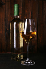 Wine bottle and wineglass with white wine on wooden background