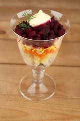 Russian herring salad in glass bowl on wooden table background