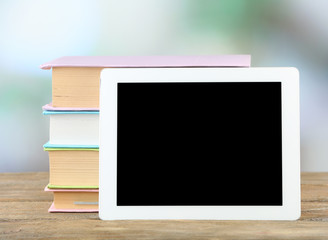 PC tablet and books on wooden table, on light background