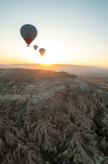 Three hot air baloons over a desert landscape at sunrise.